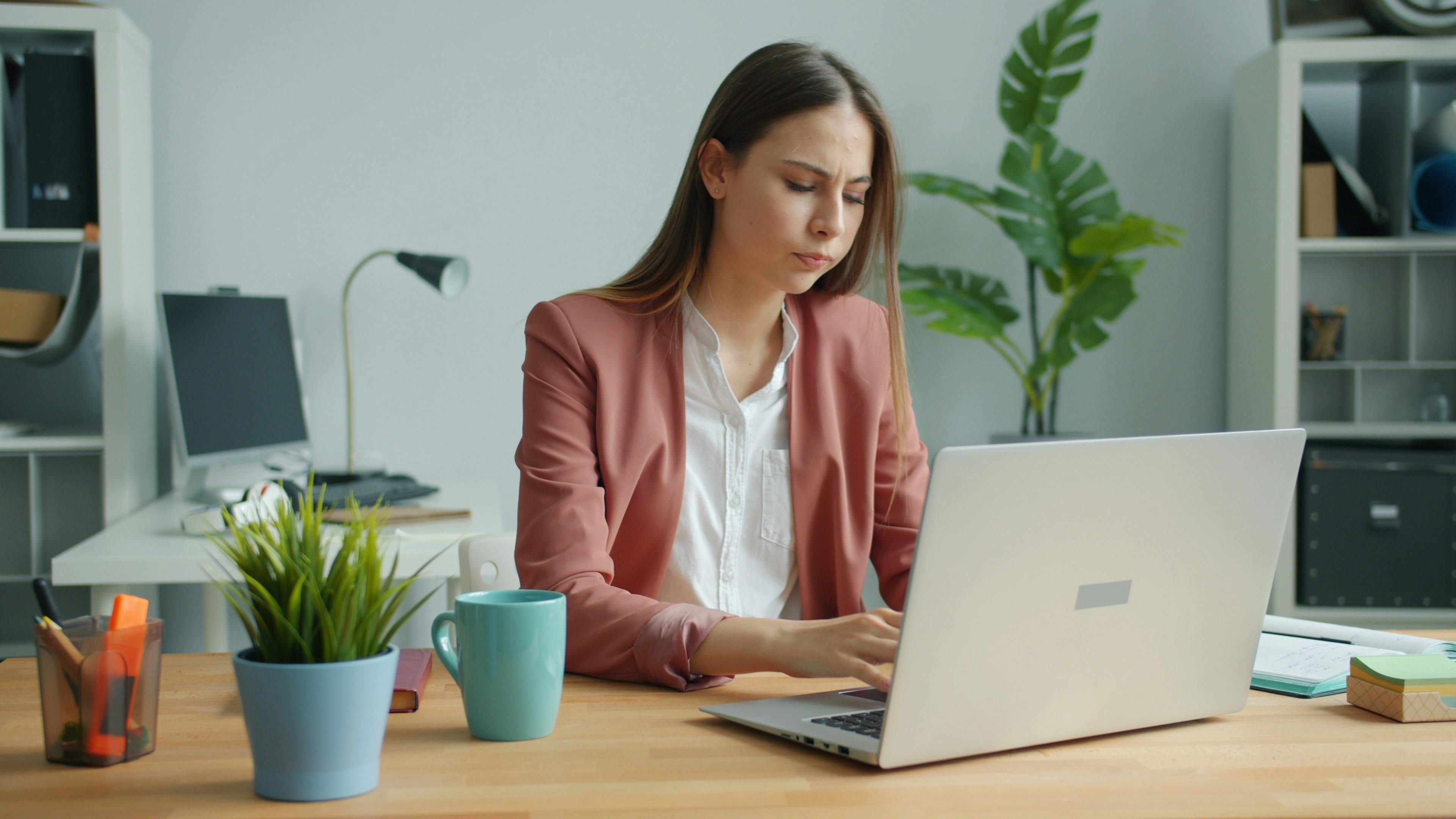 Focused young woman working at a laptop in a stylish, modern office setting.