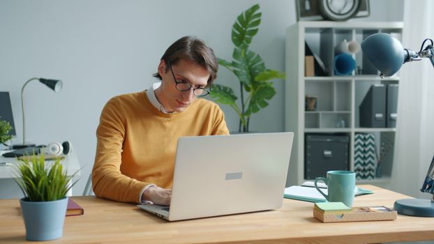 Young adult working remotely on a laptop in a modern, well-organized home office environment.