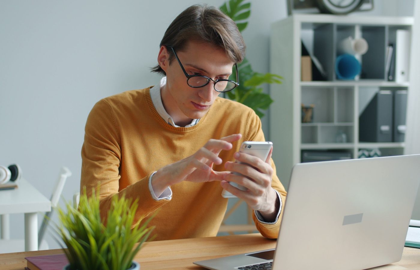 A young adult working on a smartphone and laptop in a modern office.