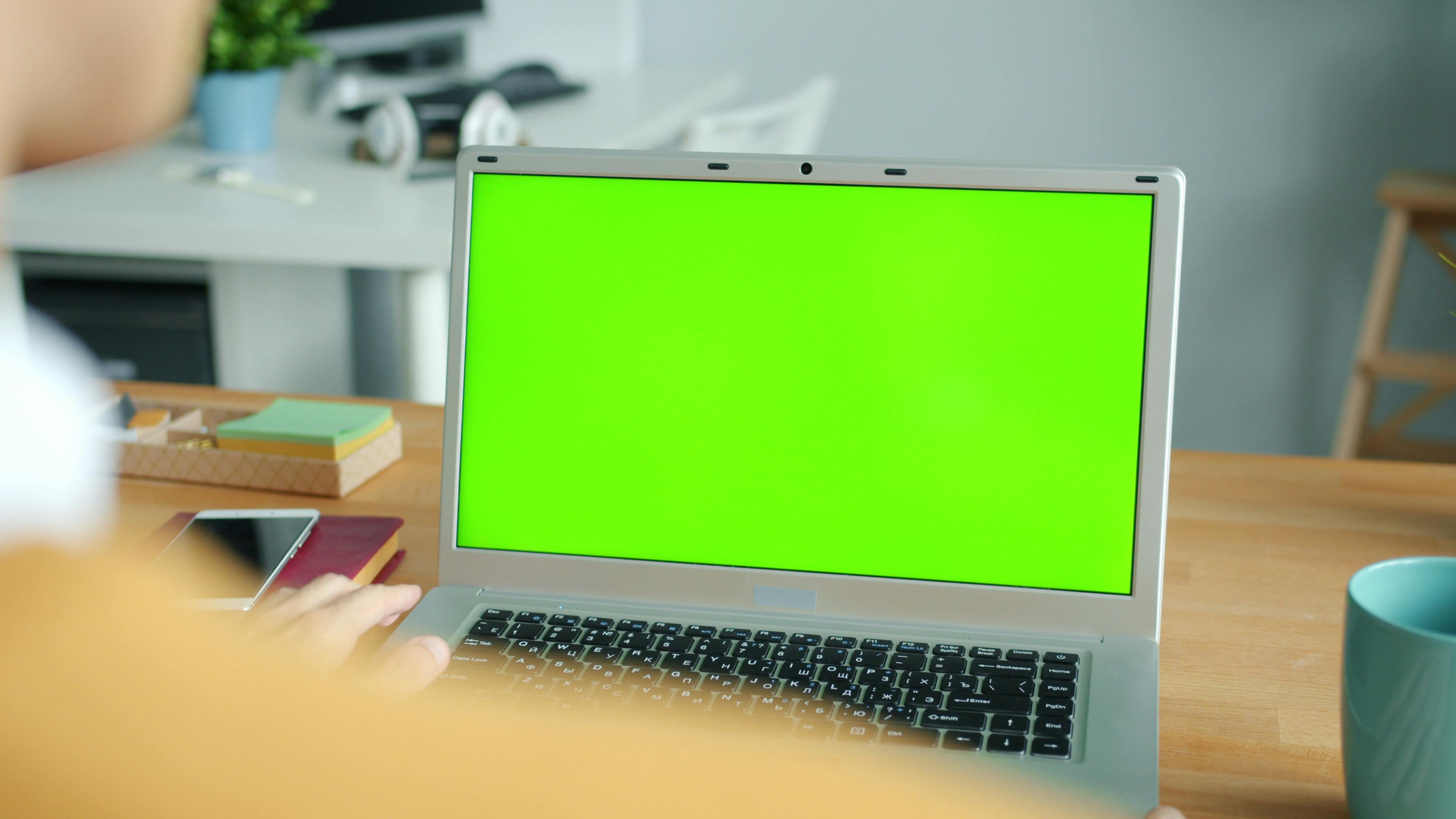 Person working on a laptop with a green screen in a modern office setting.