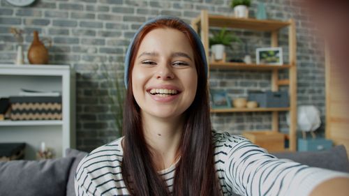 Free Cheerful young woman smiling and taking a selfie in a cozy indoor space. Stock Photo