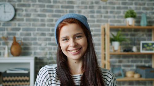 Free A happy young woman wearing a beanie smiles in a cozy indoor setting with a brick wall backdrop. Stock Photo