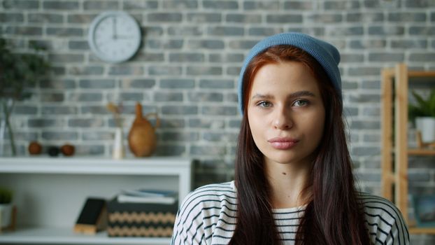 Portrait of a young woman wearing a beanie indoors with a stylish brick wall background.