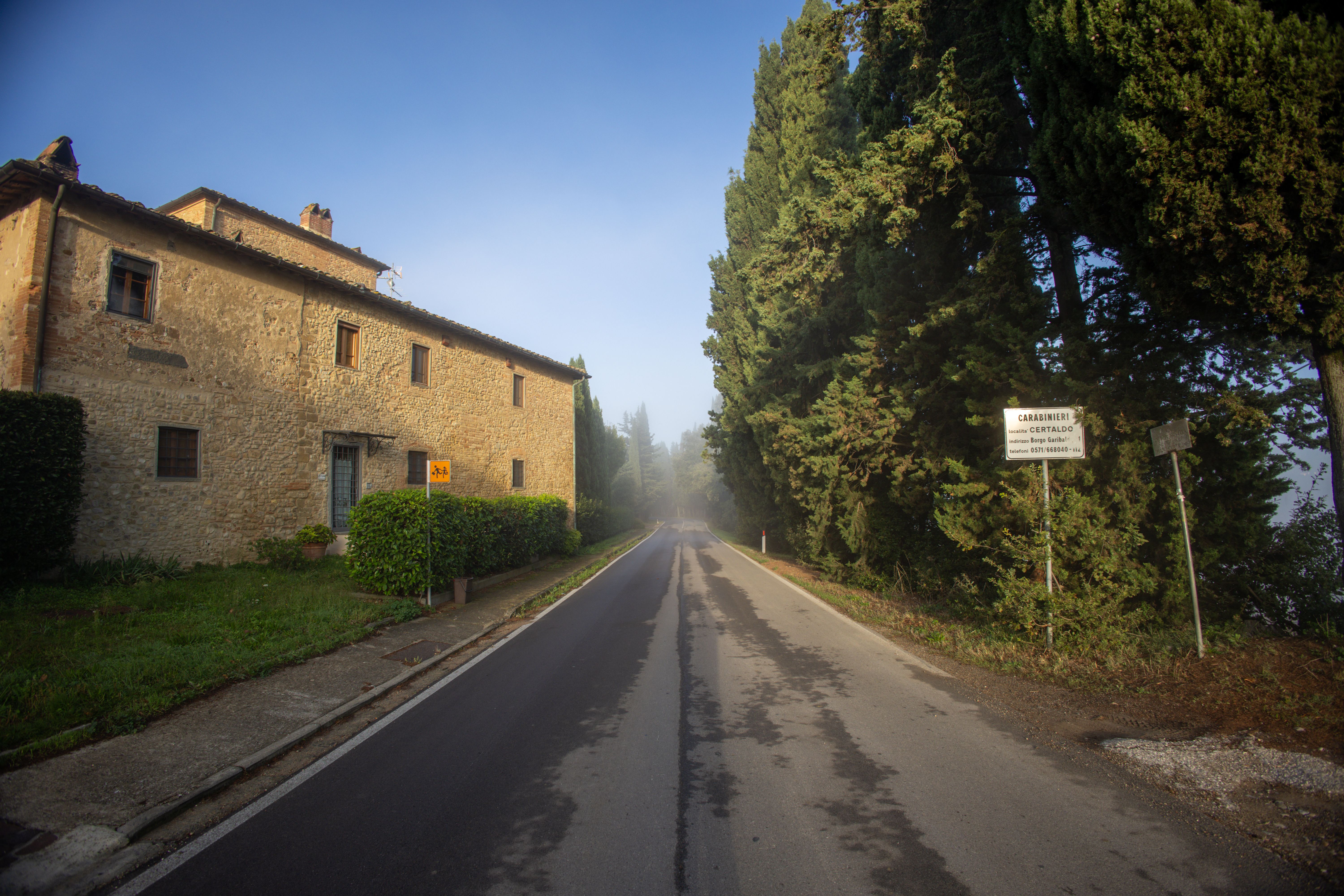 Quiet country road beside a stone house and tall cypress trees near Certaldo, Italy