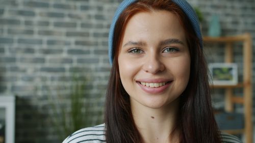 Free Portrait of a smiling young woman in a blue beanie against a brick wall background. Stock Photo
