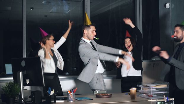 Happy office workers celebrating with party hats and blowouts in a lively indoor setting.
