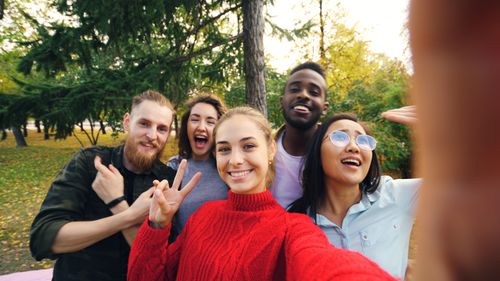 Free A multicultural group of young adults taking a cheerful outdoor selfie in a park during fall. Stock Photo