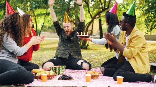 Free A group of friends celebrating a birthday outdoors with cake and party hats. Stock Photo