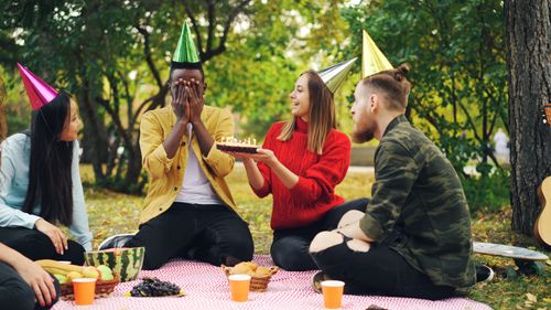 Free A group of friends celebrate a birthday outdoors with cake and party hats. Stock Photo