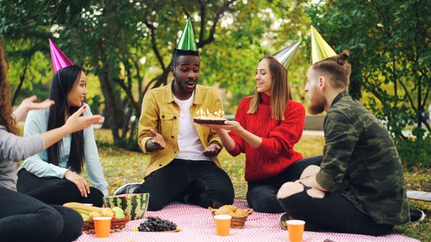 Group of friends celebrating a birthday with cake and party hats in a park.