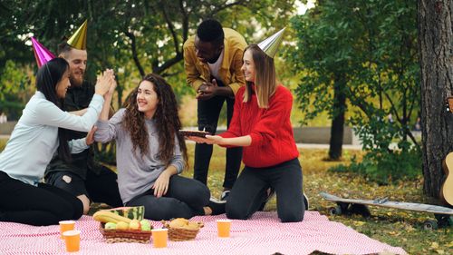 Free Group of friends enjoying a lively outdoor picnic party with hats and snacks. Stock Photo