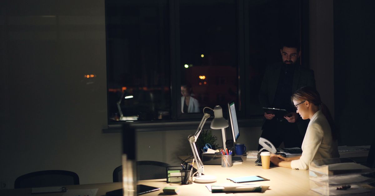 Dos profesionales trabajando hasta tarde en una oficina poco iluminada, centrados en las tareas.