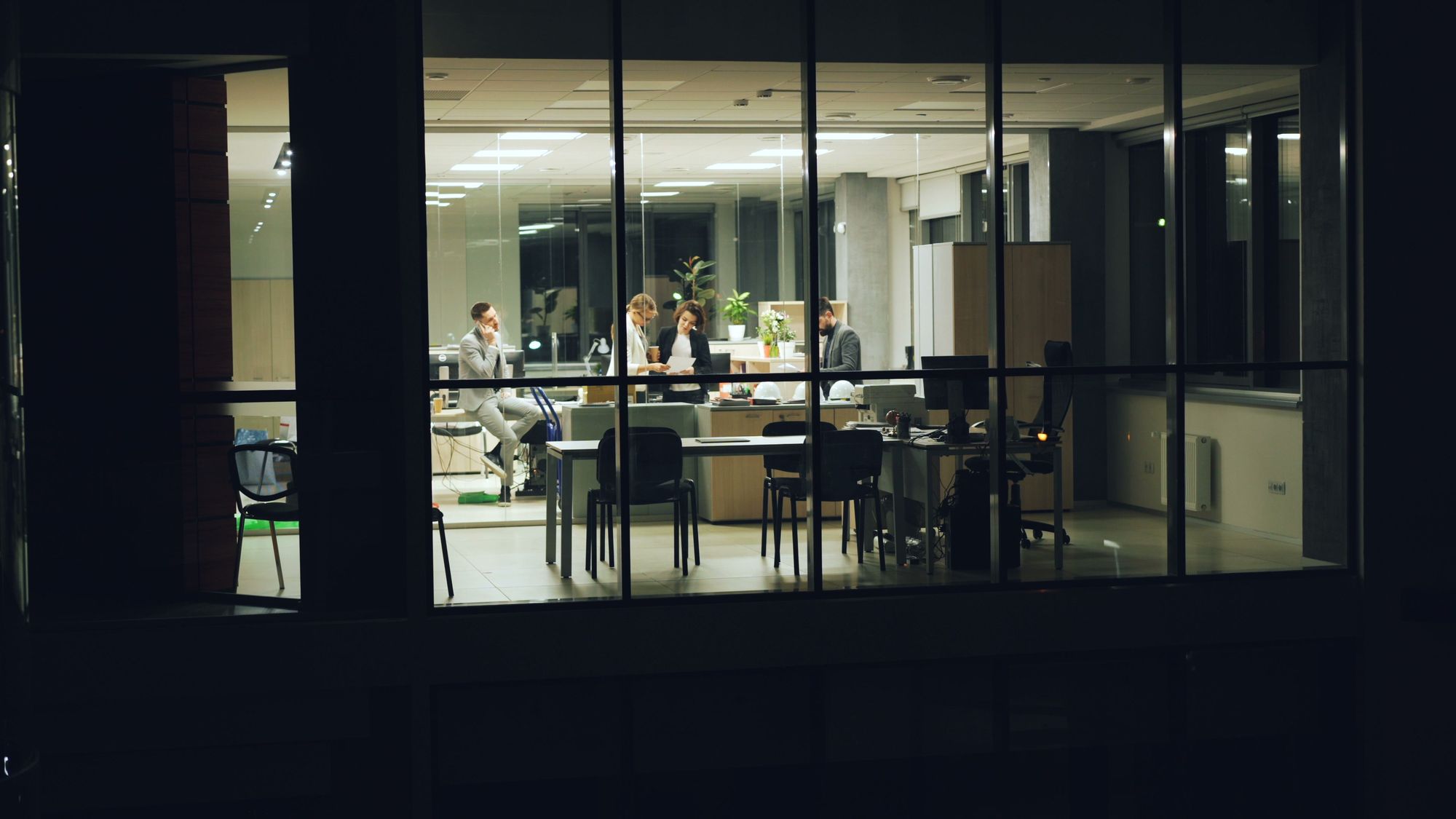 Colleagues working late in a glass-walled office — photo by Vitaly Gariev on Pexels