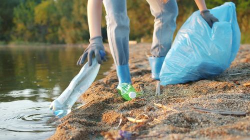 Free Person collecting plastic waste on a beach, promoting environmental conservation. Stock Photo
