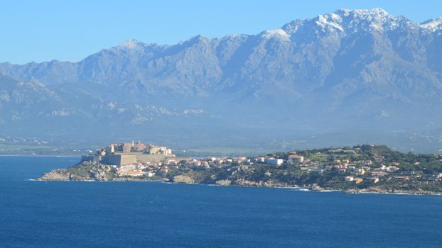 A stunning view of Calvi, Corsica with mountains in the background and the Mediterranean Sea.