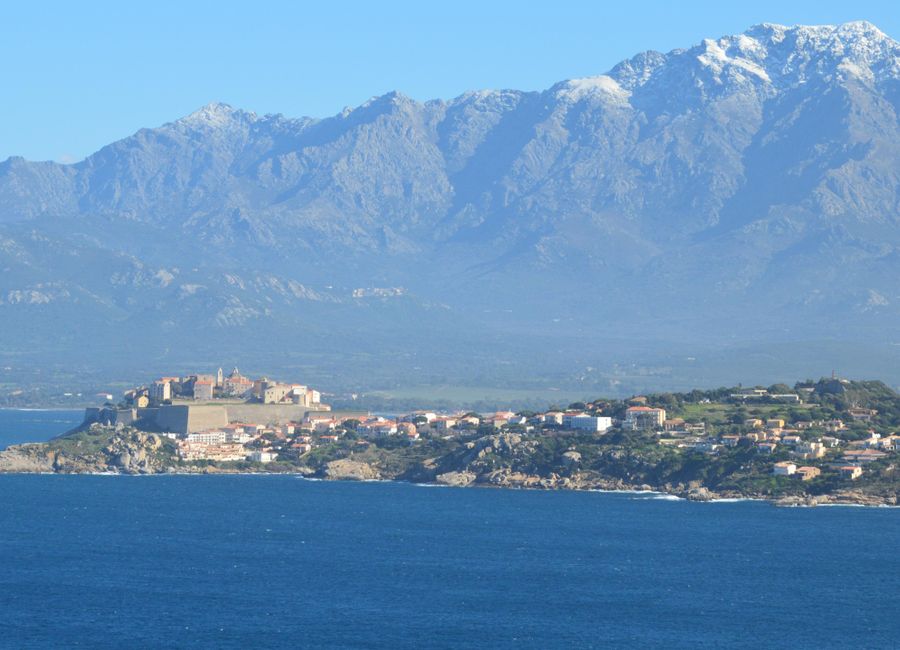 A stunning view of Calvi, Corsica with mountains in the background and the Mediterranean Sea.