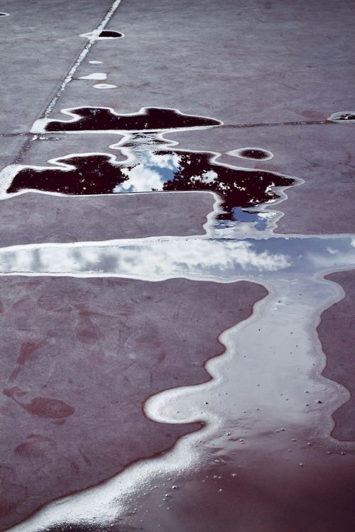 Free Pavement puddles reflecting blue sky and clouds, creating an abstract artistic view. Stock Photo