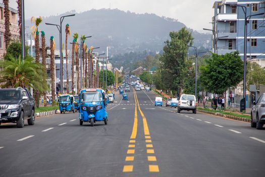 Busy street in Gondar, Ethiopia with blue tuk-tuks, palm trees, and mountain backdrop.