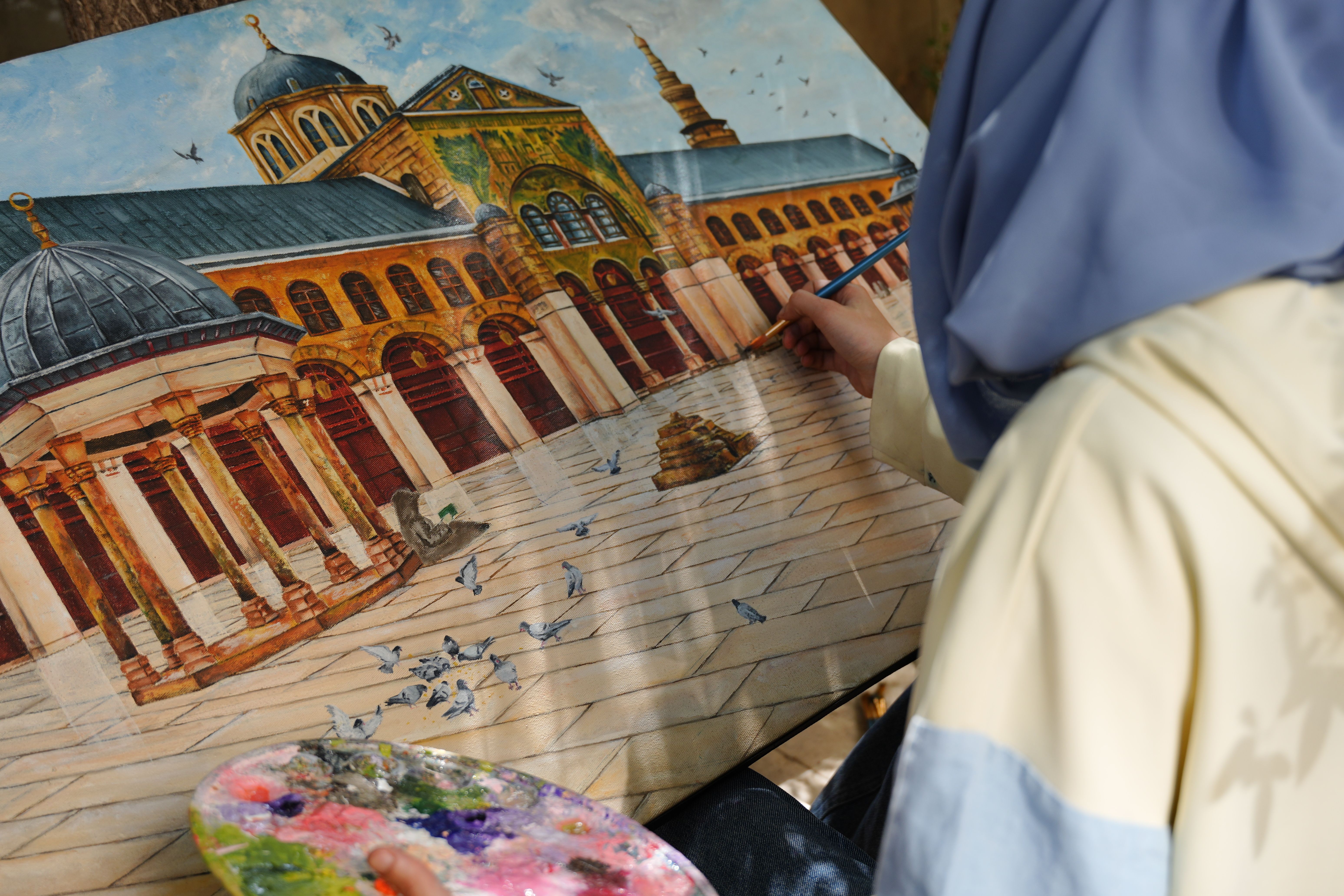 Gratis En kunstner maler den ikoniske Umayyad-moské i Damaskus, mens han sidder udendørs, og indfanger arkitektoniske detaljer. Lagerfoto