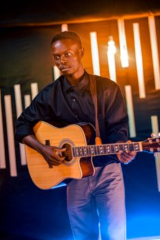 A young man performs passionately on guitar under warm stage lights.