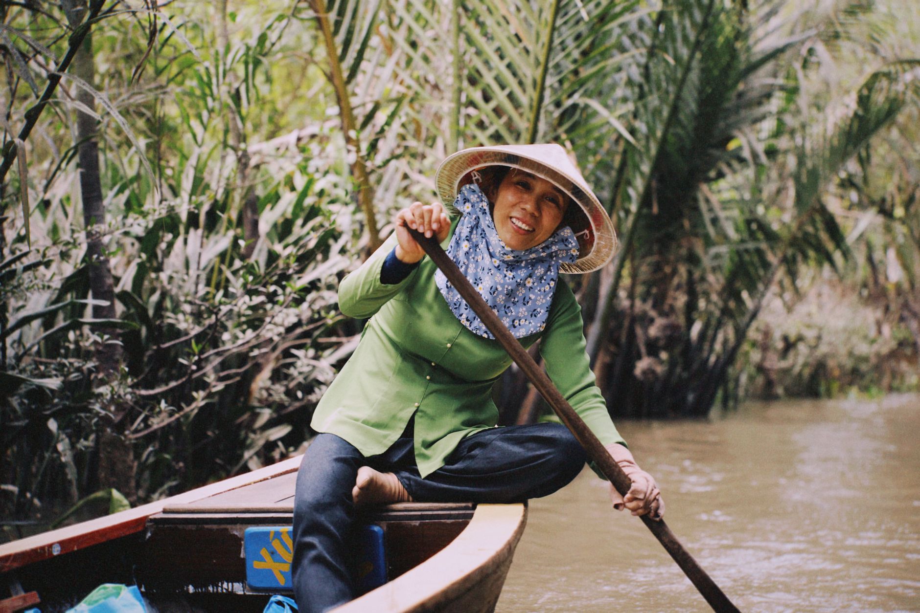 A Vietnamese woman in traditional attire rowing a boat through the lush Mekong Delta.