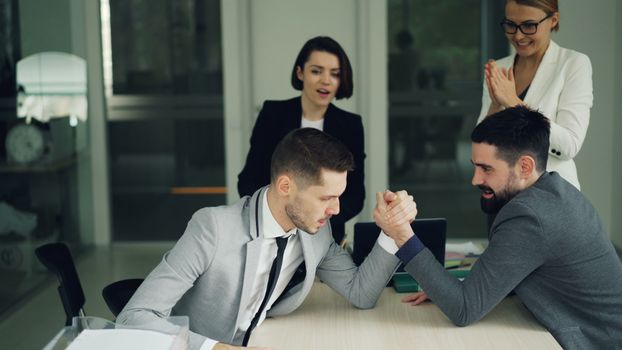 Colleagues cheering for a friendly office arm wrestling match among team members.