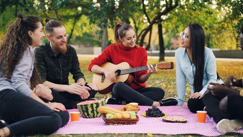 Free Group of friends having a picnic in the park, playing guitar and enjoying food. Stock Photo