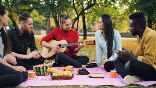 Free Group of diverse friends having a picnic outdoors with music and snacks. Stock Photo