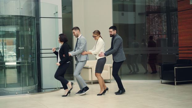 Business professionals enjoy conga line fun in modern office setting.