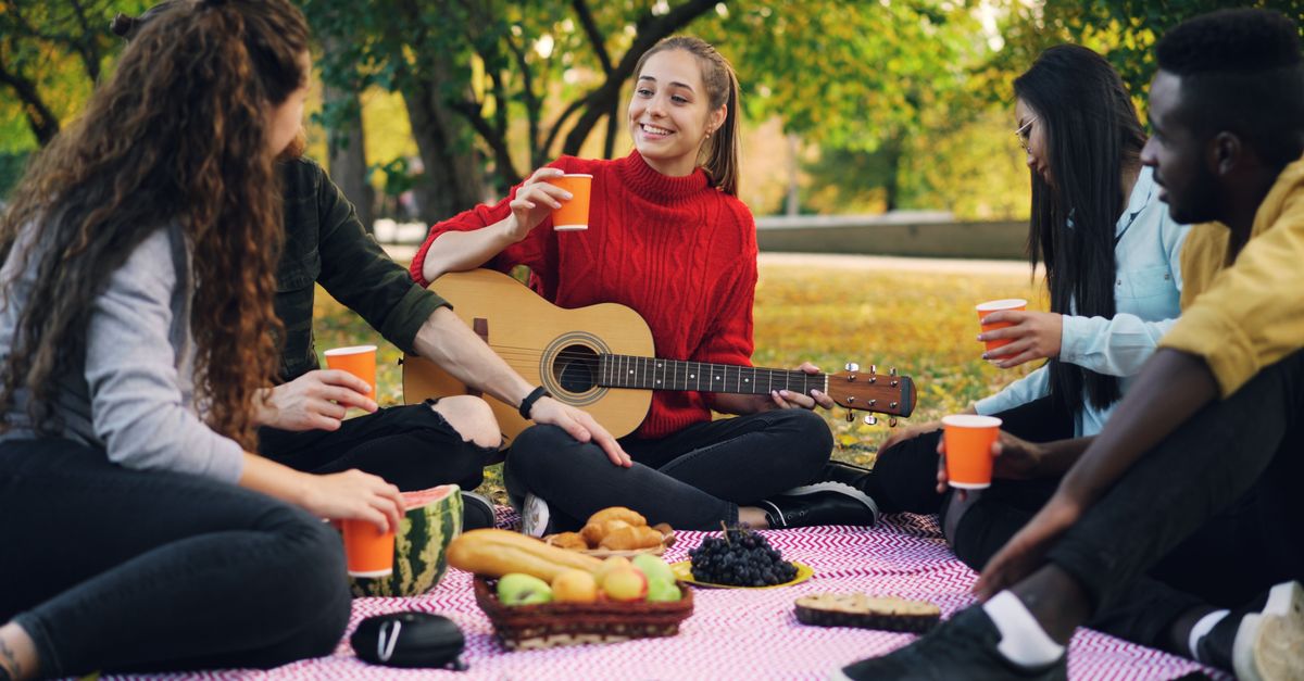 A group of diverse friends laughing while having a picnic in the park instead of an expensive restaurant