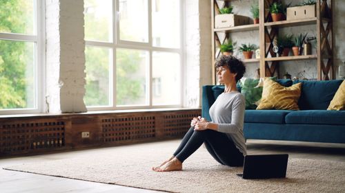 Free A woman meditating indoors with natural light, surrounded by plants. Stock Photo
