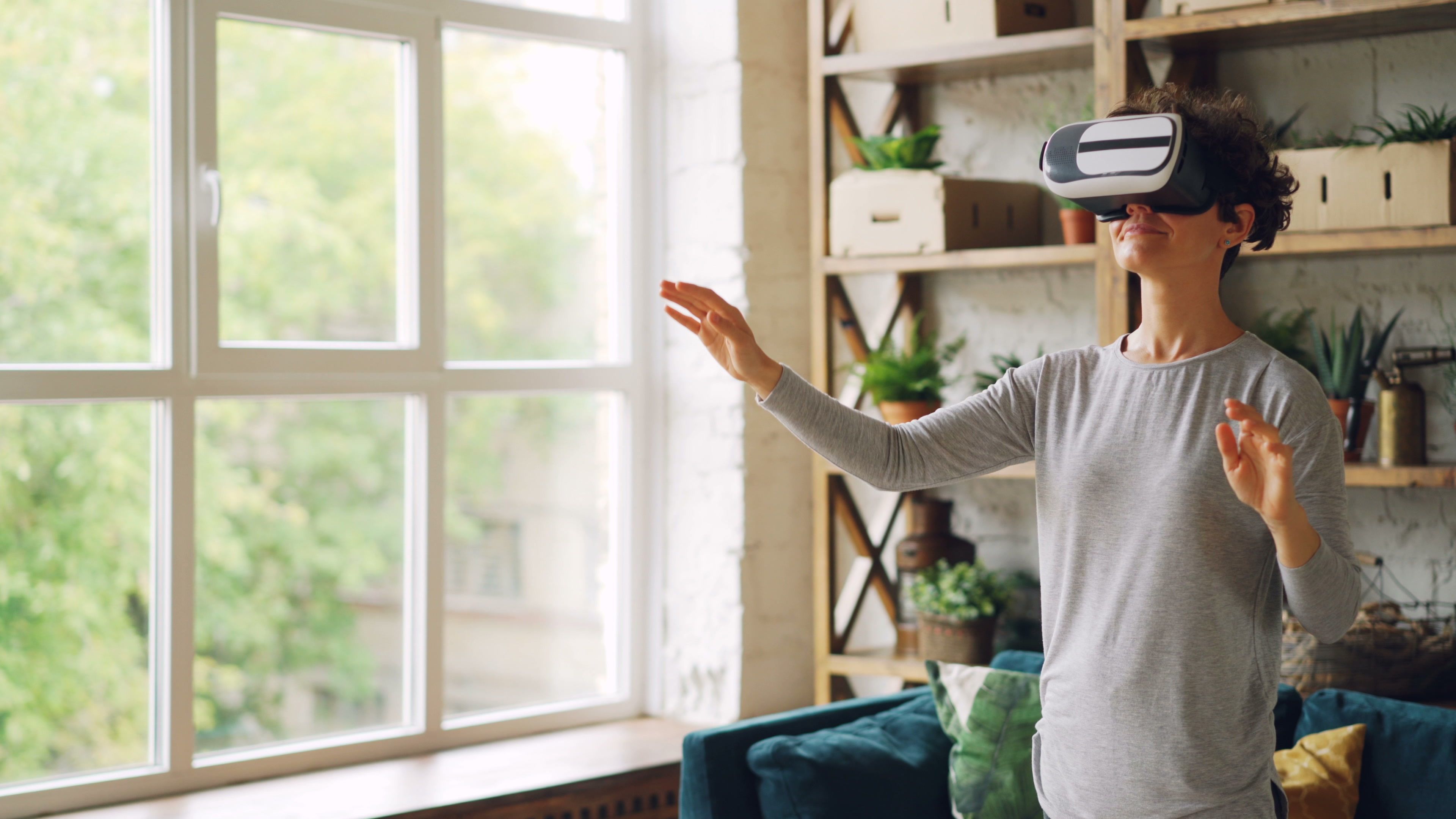 An adult woman wearing VR goggles, interacting with virtual reality in a modern indoor setting.