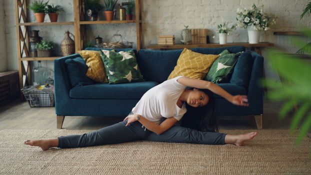 Woman practicing yoga indoors, performing side stretch on floor. Cozy and serene home environment.