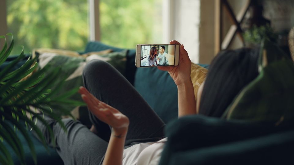 Woman relaxing on a couch, engaged in a video call on her smartphone, indoors.