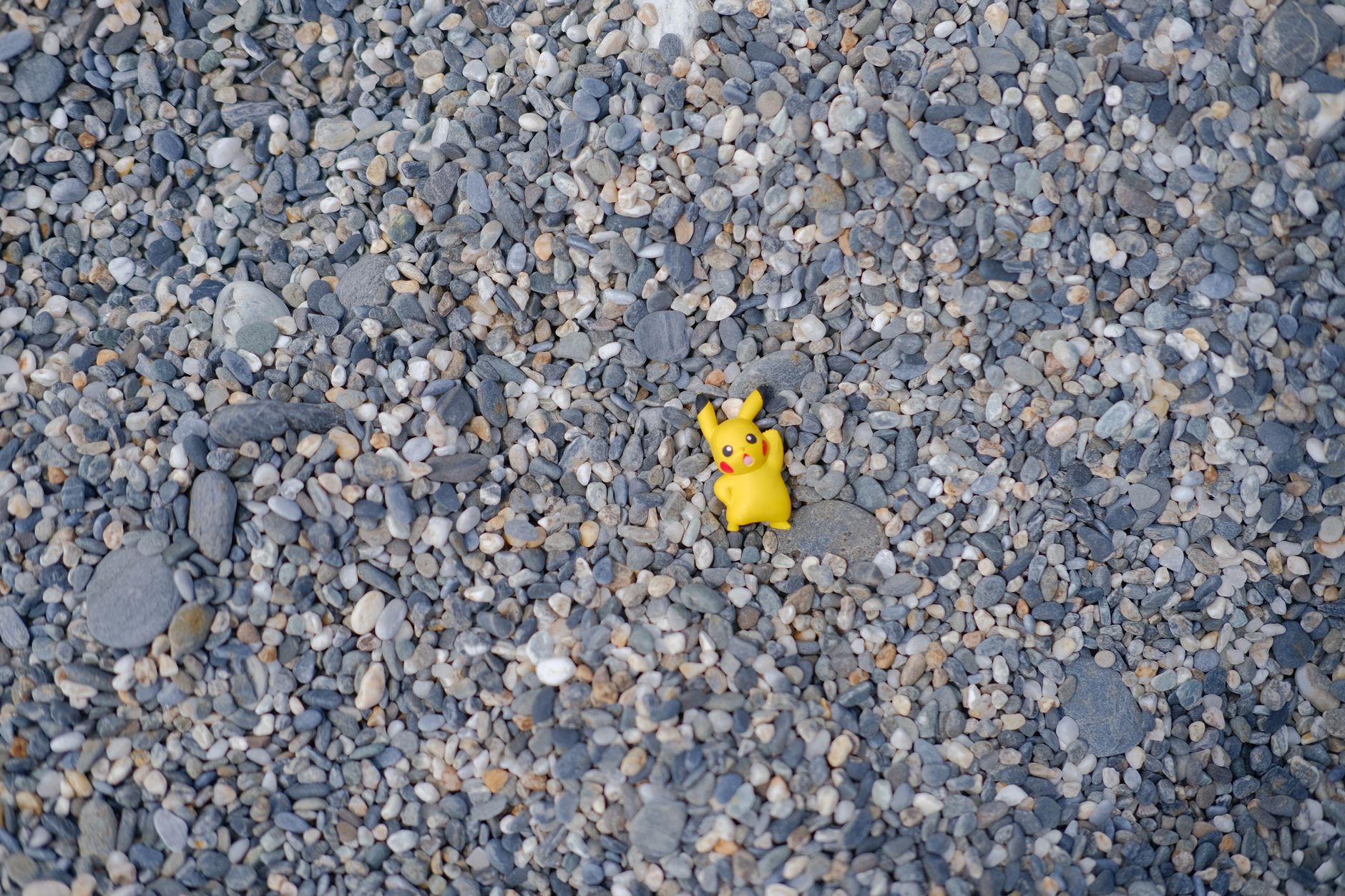 A bright yellow Pikachu toy sits on a pebble-covered beach in Taiwan.