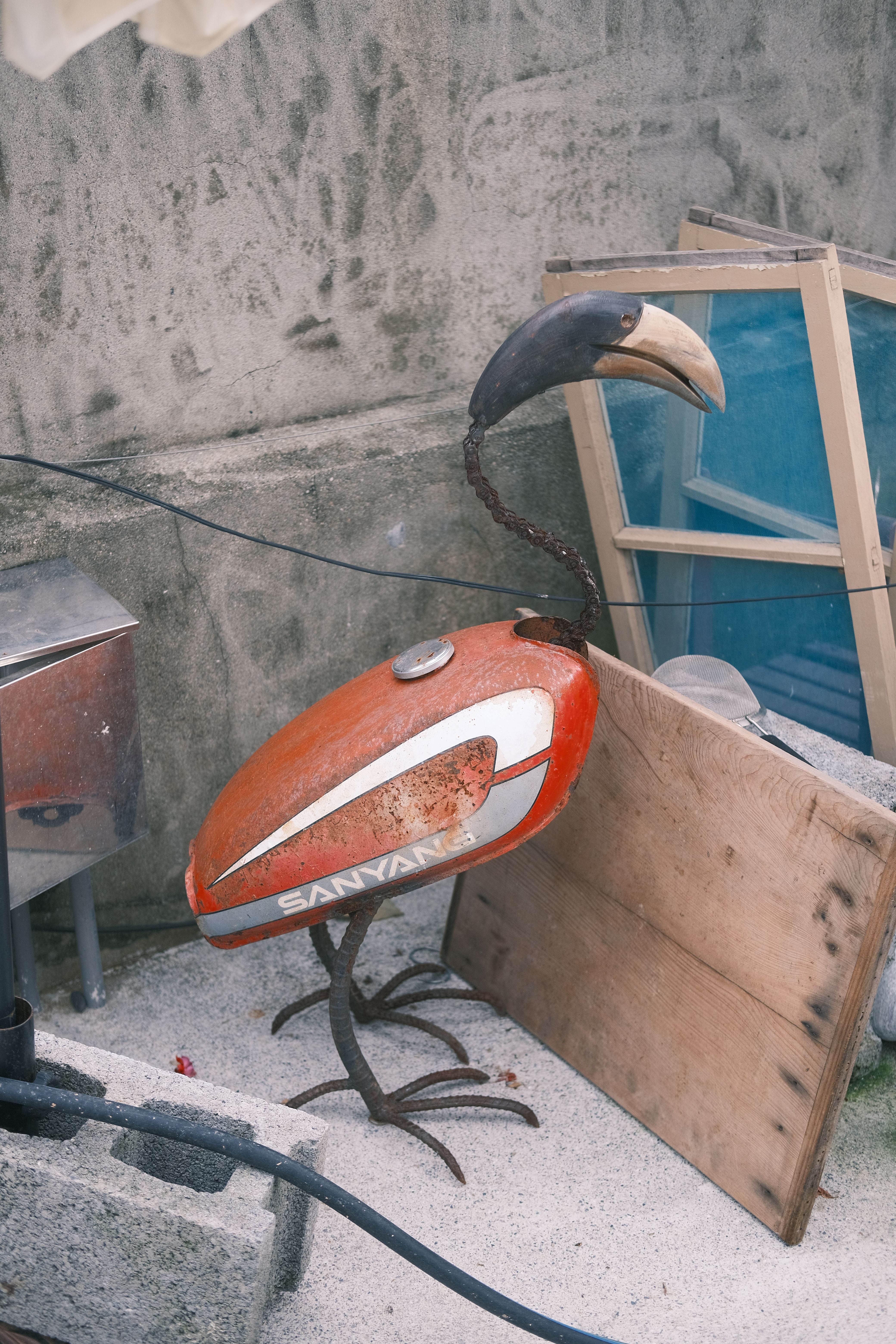 Artistic metal flamingo sculpture made from repurposed objects in an outdoor setting, showcasing creativity.