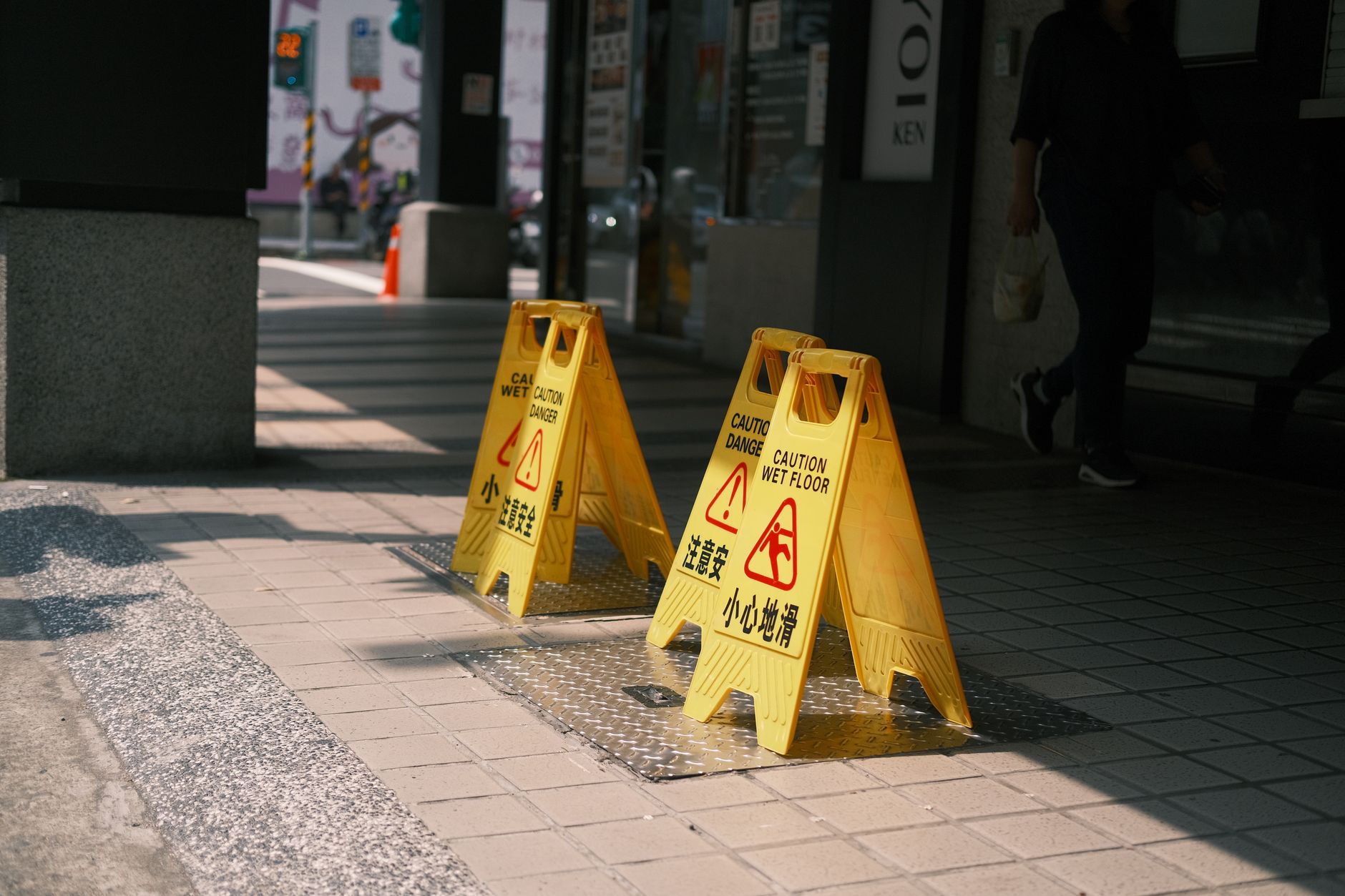 Yellow caution wet floor signs on a sunlit outdoor sidewalk, indicating a safety warning.