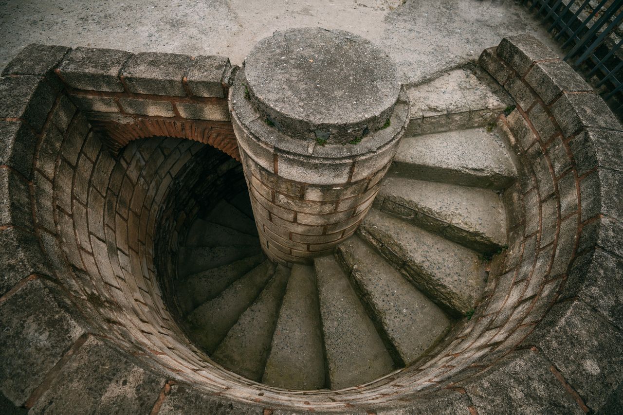 Top view of a spiraling stone staircase outdoors, showcasing architectural beauty.