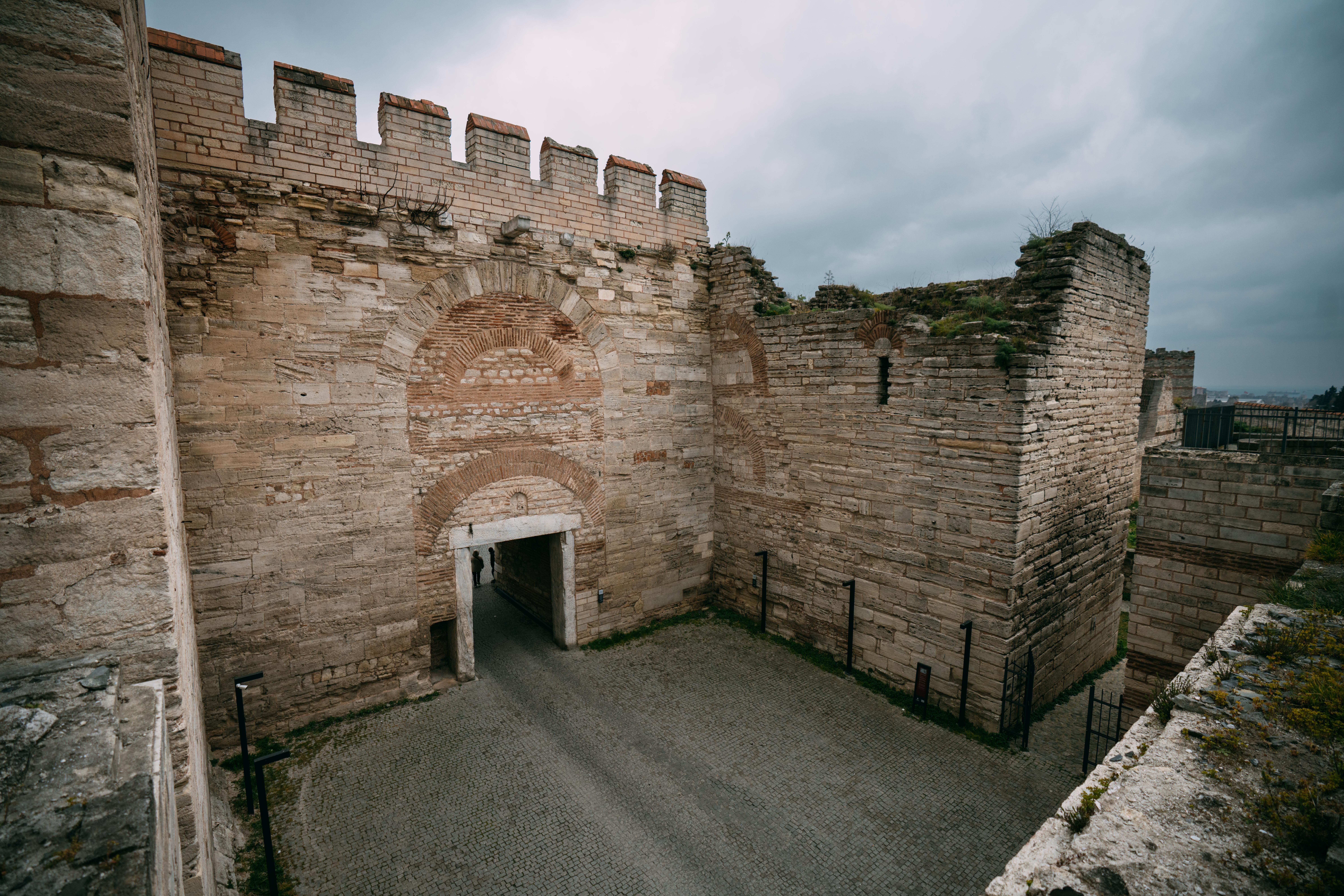 Old stone fortification passage with weathered walls under cloudy skies, showcasing historical architecture.