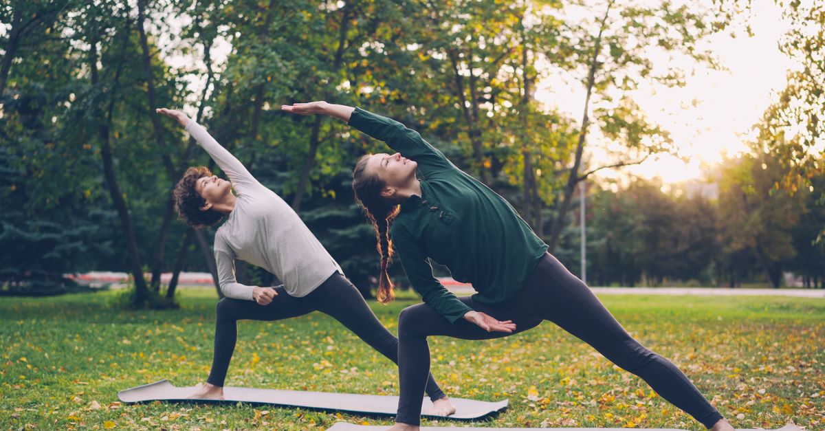 Two women practicing yoga outdoors in a tranquil park during sunset.