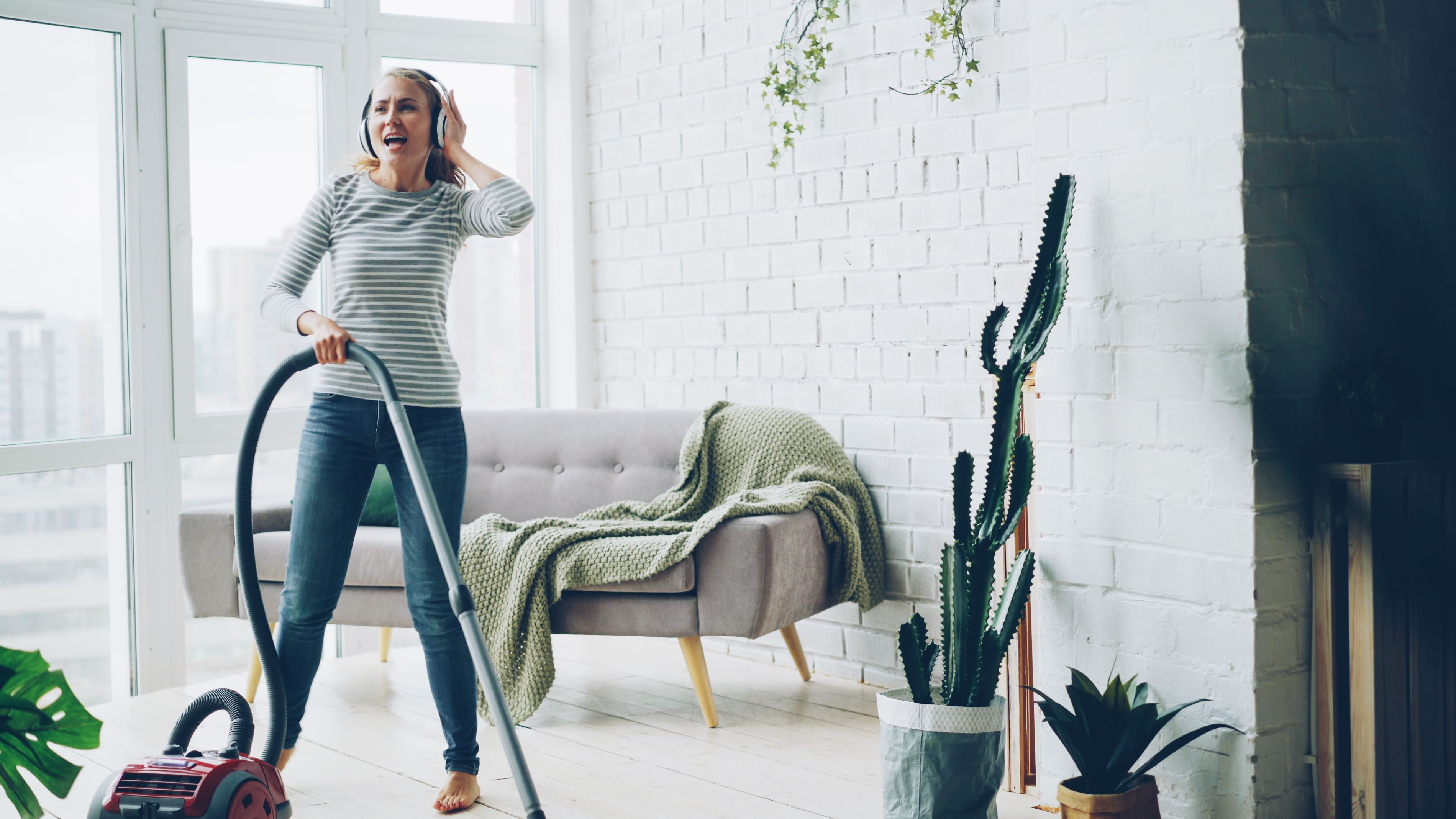 Cheerful woman vacuuming indoors while listening to music.