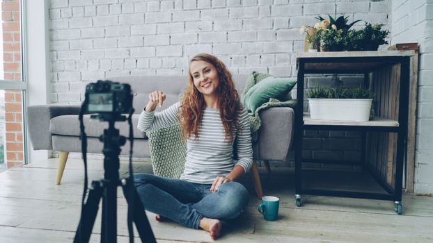 Smiling woman sitting on floor, recording video in cozy room.