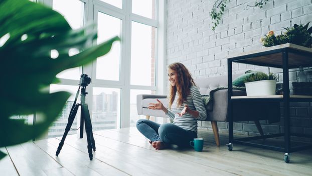 Woman vlogging indoors near window, casual setup with plants.