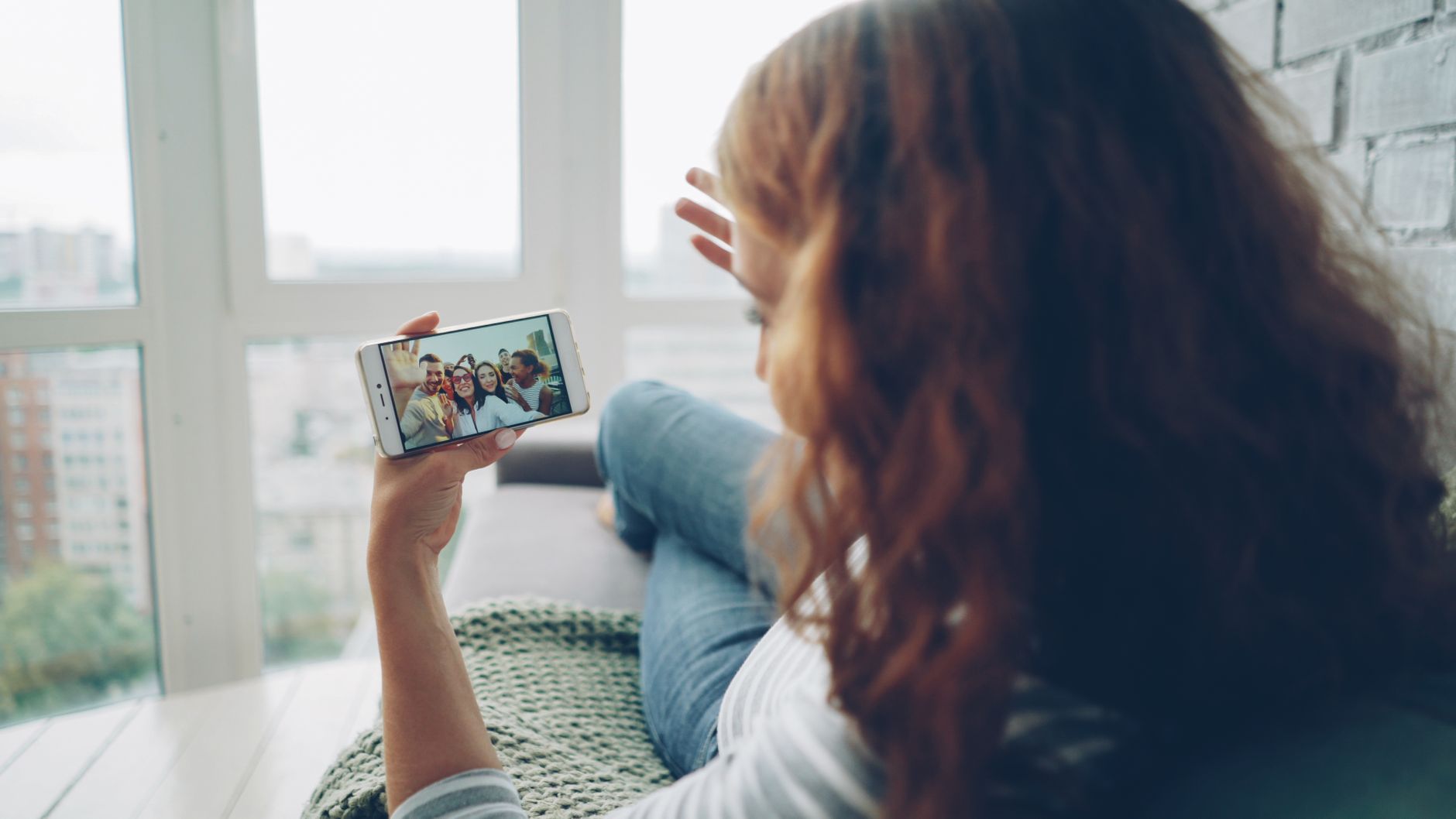 Woman relaxing indoors while video chatting with friends on smartphone.