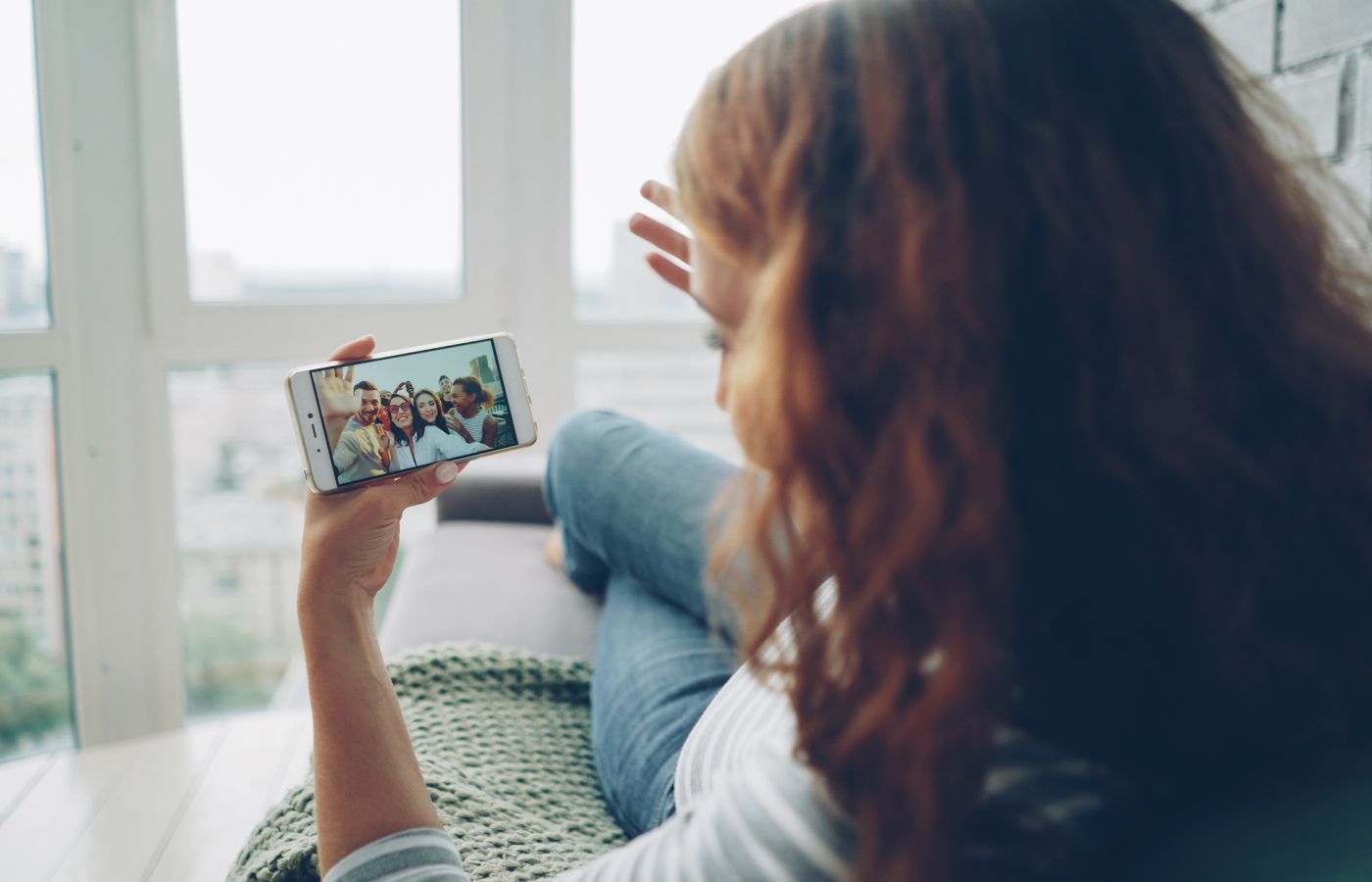 Woman relaxing indoors while video chatting with friends on smartphone.