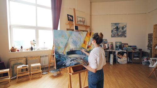 Free A female artist painting a vibrant seascape on canvas in a well-lit studio. Stock Photo