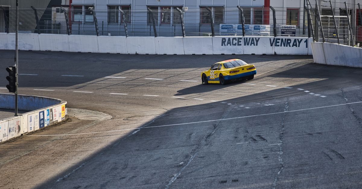 A yellow race car speeding on the track at Raceway Venray under clear skies.