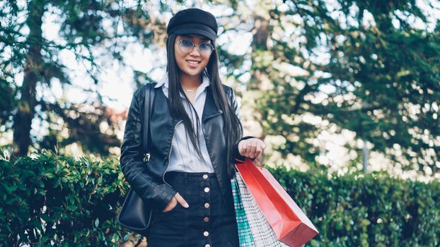 Trendy woman enjoys shopping outdoors with vibrant bags during daylight.