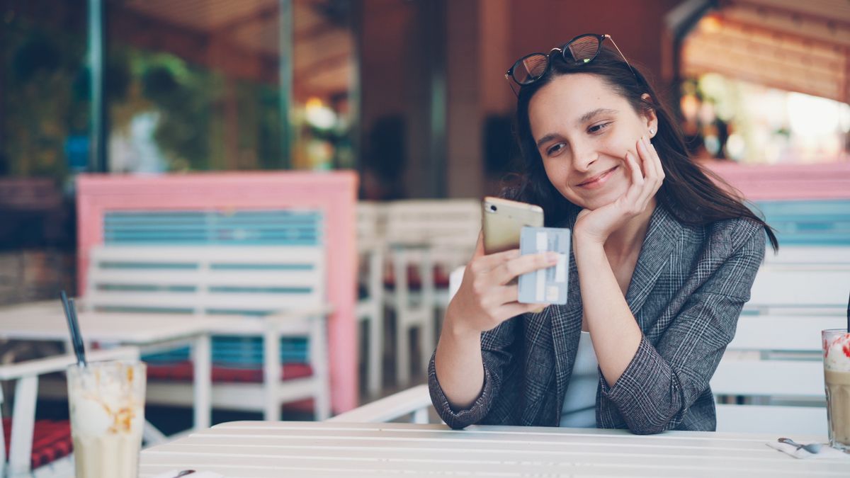 Elinde akıllı telefon tutan genç bir kadın, renkli bir kafede oturuyor