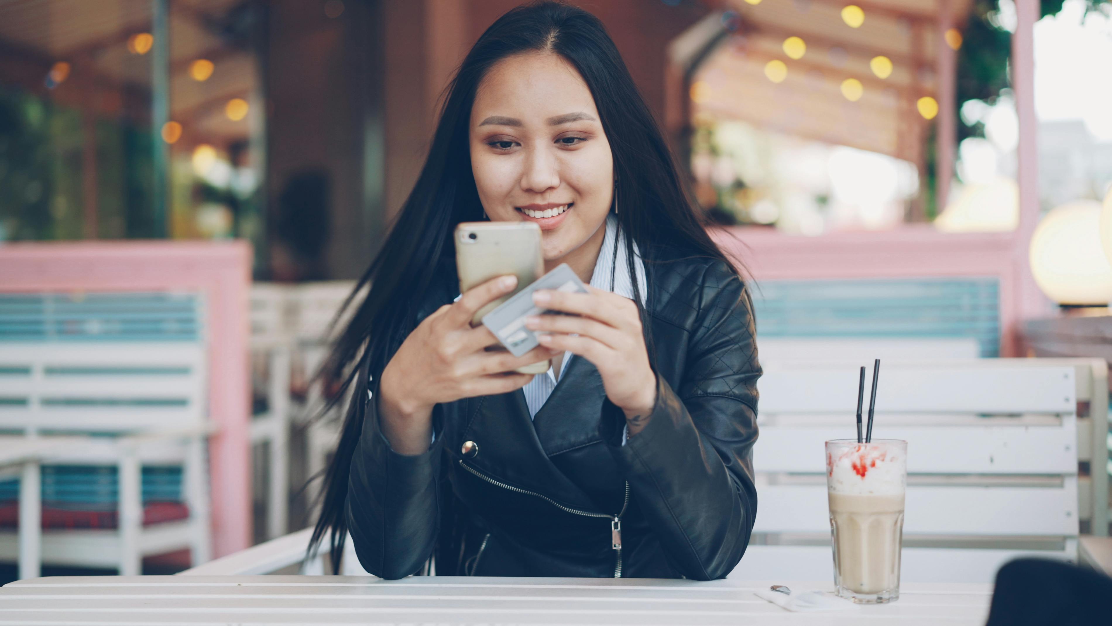 Latina woman smiling while using a credit builder app on her smartphone at a coffee shop